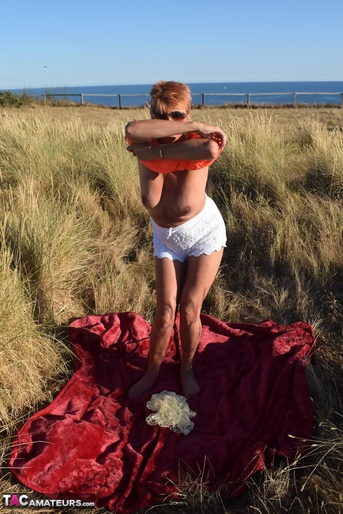 Fit older lady Dimonty exposes big naturals on a blanket overlooking the ocean page 1